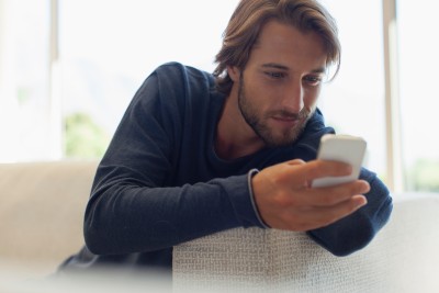 mann lehnt an ecke der couch mit seinem handy in der hand