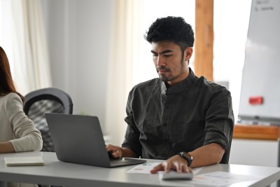 mann sitzt am schreibtisch und schaut auf den laptop