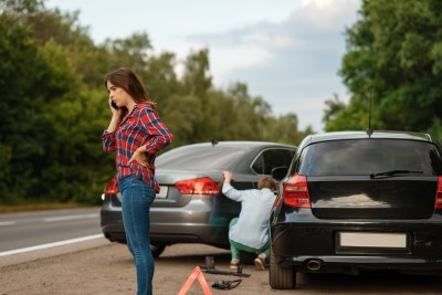 frau telefoniert während ein mann sich die verunfallten fahrzeuge anschaut