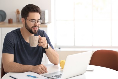 mann sitzt am schreibtisch vor laptop mit tasse in der hand
