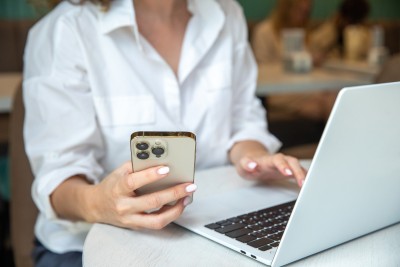 frau sitzt am laptop und hält handy in der hand