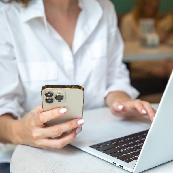 frau sitzt am laptop und hält handy in der hand