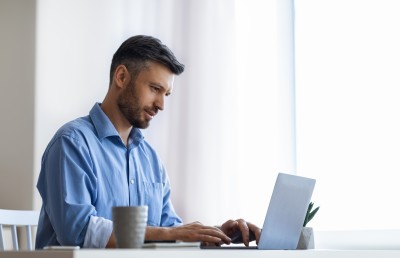 mann mit blauem hemd sitzt am schreibtisch und tippt am laptop
