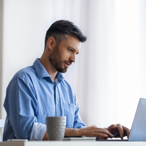 mann mit blauem hemd sitzt am schreibtisch und tippt am laptop