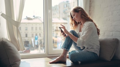 frau sitzt am fenster mit ihrem handy in der hand