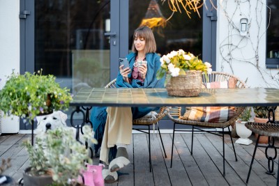 frau sitzt auf der terasse am tisch mit tasse und handy in der hand