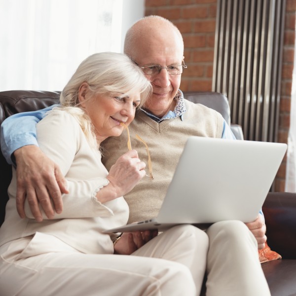 rentnerpaar sitzt auf dem sofa mit einem laptop auf dem schoss