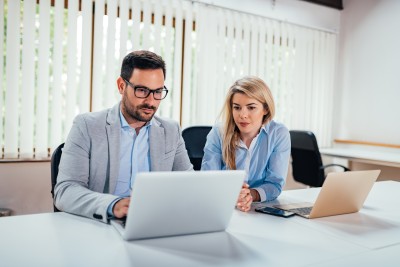 zwei personen sitzen am schreibtisch und schauen auf einen bildschirm