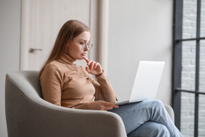 frau sitzt auf einem sessel mit laptop auf dem schoss und recherchiert