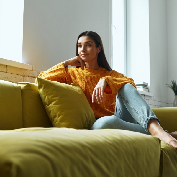 frau sitzt auf dem sofa und wirkt nachdenklich