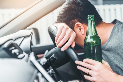 mann sitzt am steuer eines fahrzeugs mit bierflasche in der hand und lehnt ans lenkrad