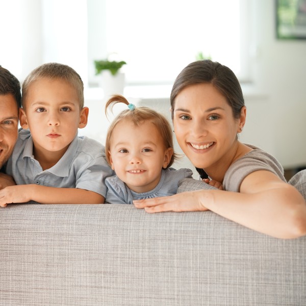 famiile sitzt auf dem sofa und schaut über die rückenlehne in die kamera