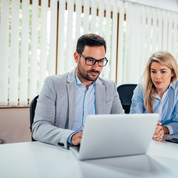 zwei personen sitzen am schreibtisch und schauen auf ein laptop