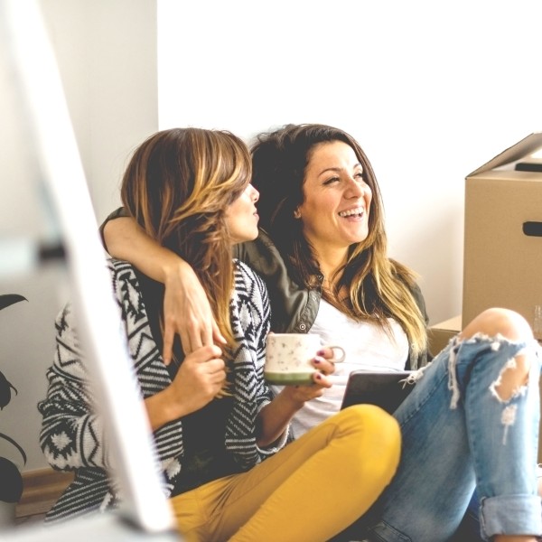zwei frauen sitzen auf dem boden neben kartons und lachen