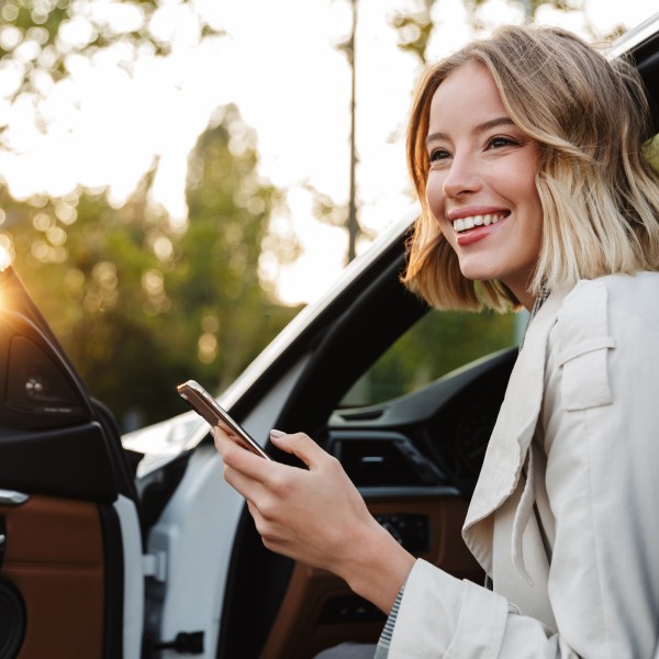 frau steigt mit handy in der hand aus dem auto