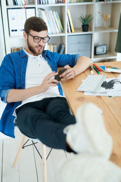 Man mit Handy in der Hand und Füßen auf Schreibtisch
