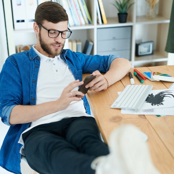 Man mit Handy in der Hand und Füßen auf Schreibtisch