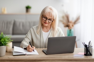 Frau sitzt vor Notbook und macht sich Notizen