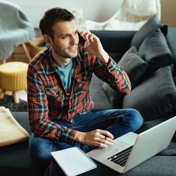 Mann telefoniert auf Sofa mit Notebook vor ihm
