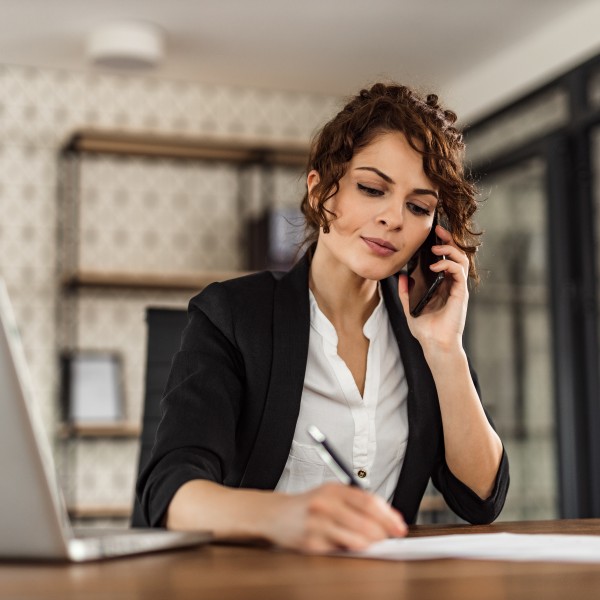 Frau telefoniert und macht sich Notizen