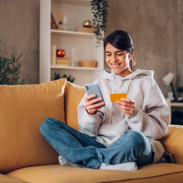 Frau sitzt auf dem Sofa mit Handy und Kreditkarte