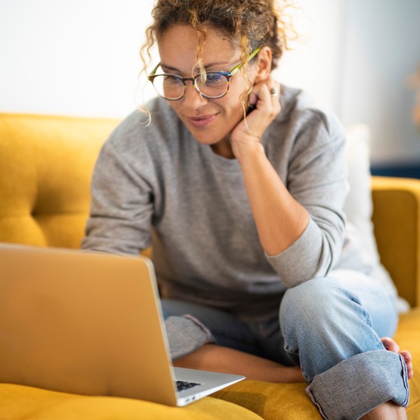 Frau sitzt auf gelbem Sofa am Laptop