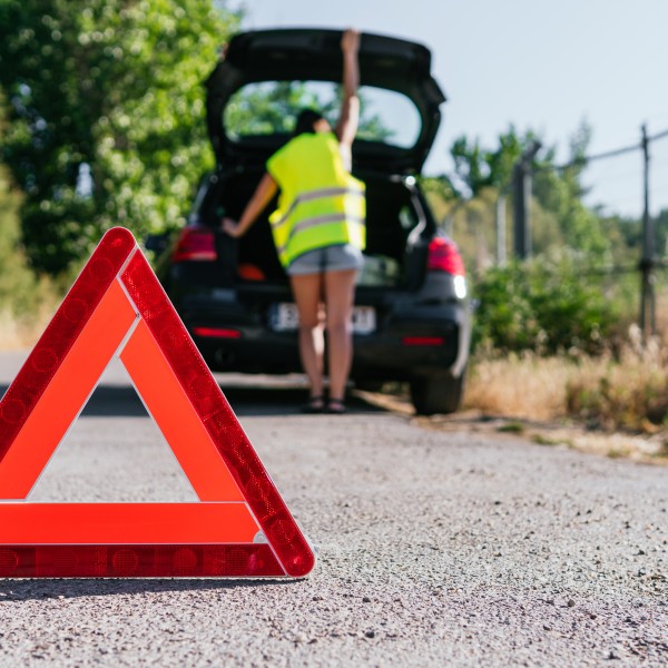 Frau mit Warnweste am Kofferraum, nachdem sie das Warndreieck aufgestellt hat