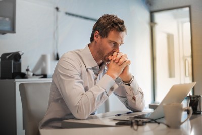 Mann sitzt mit verschränkten Händen vorm Laptop